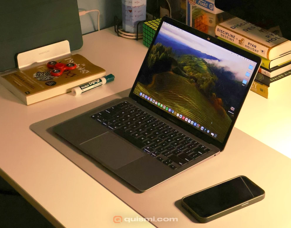 MacBook Pro on a desk displaying elegant screen saver, surrounded by books and accessories.